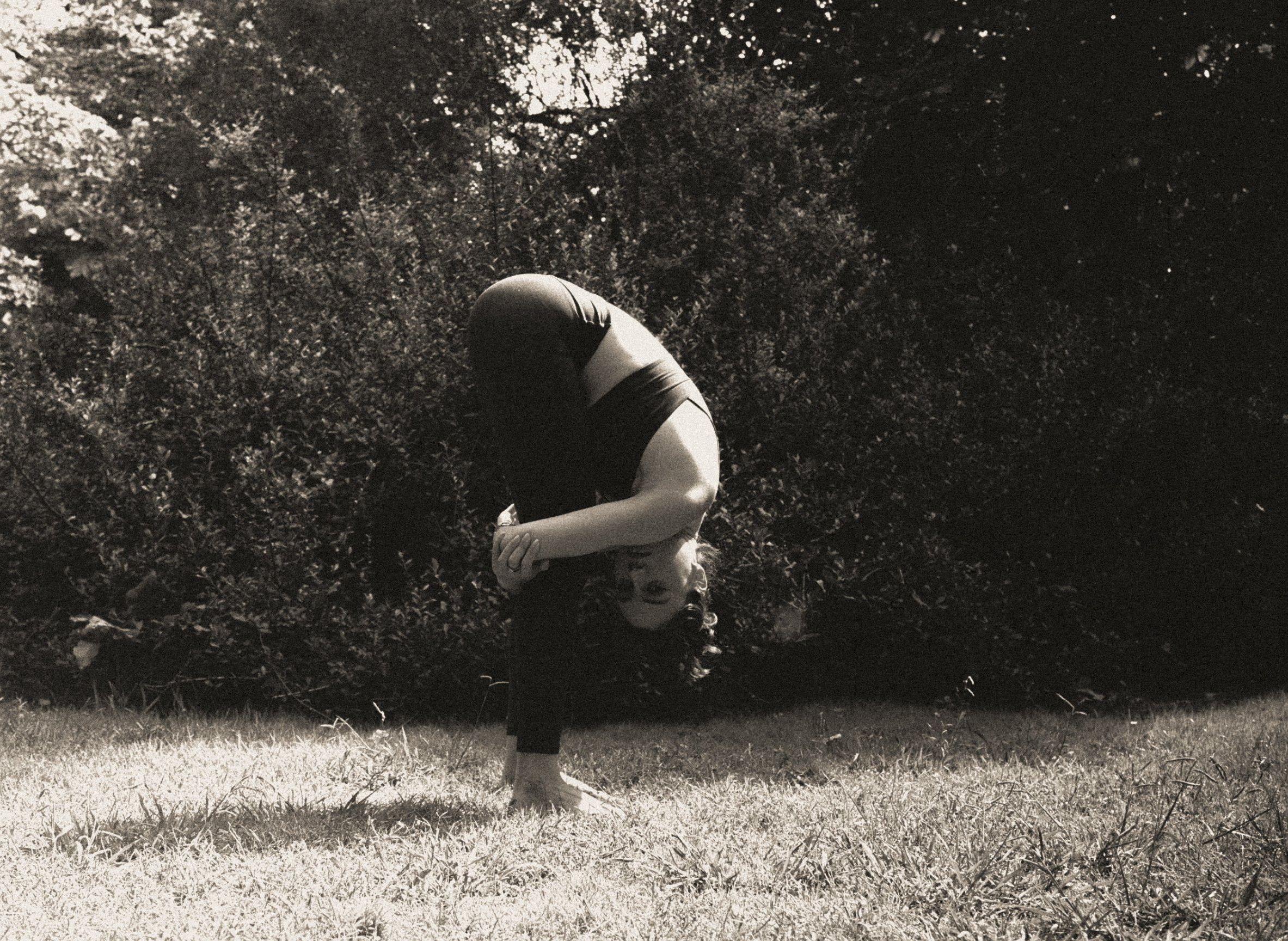 Emilia en una postura de yoga de apertura de pecho al aire libre, entre árboles; fotografía en blanco y negro